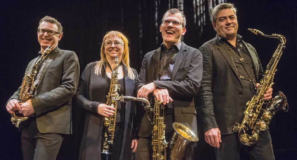 Four musicians with saxophones smile on stage.