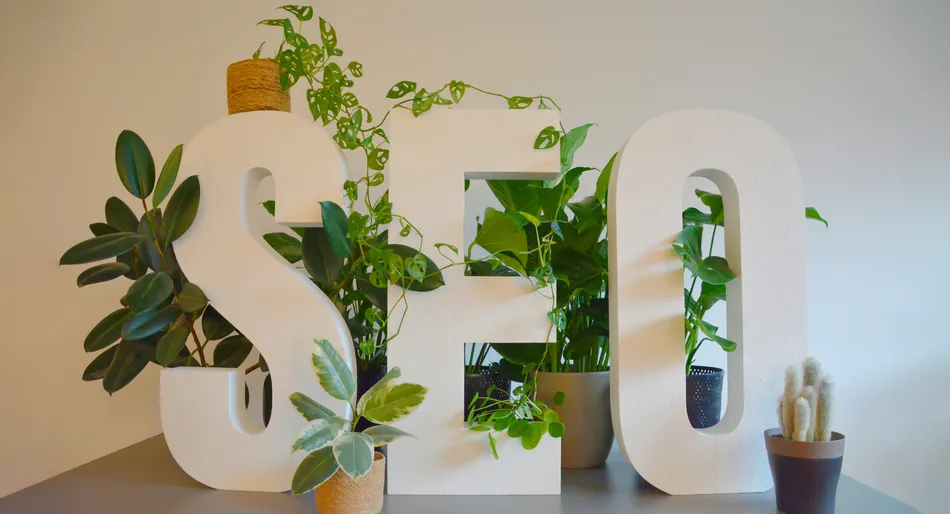 "Lettres SEO blanches devant des plantes vertes sur une table grise."